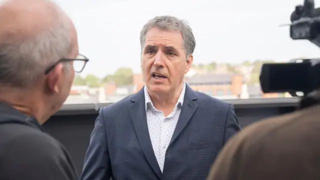 Liverpool City Region mayor Steve Rotheram, with short grey hair, is wearing a shirt and blazer while speaking to the media