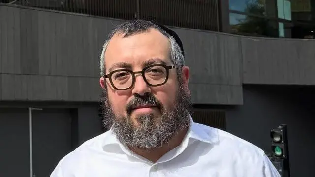 A man with black-rimmed glasses and a grey beard looks at the camera.