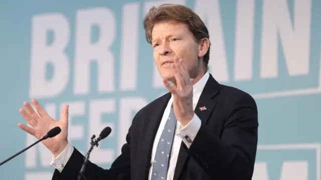 Reform UK deputy leader Richard Tice at a news conference wearing a dark suit, white shirt and blue tie