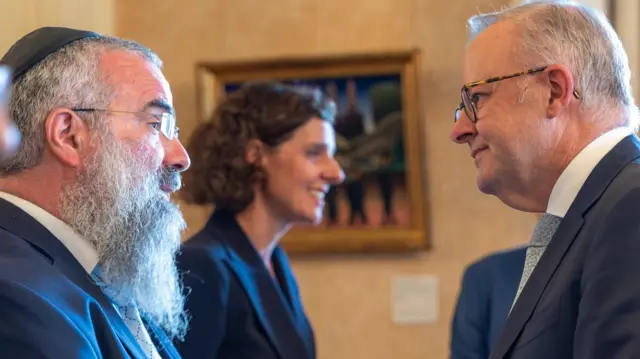 Albense speaking to a man with grey beard wearing a kippah