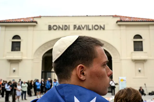 A man draped in an Australian flag and wearing a kippah stands in front of the Bondi Pavillion