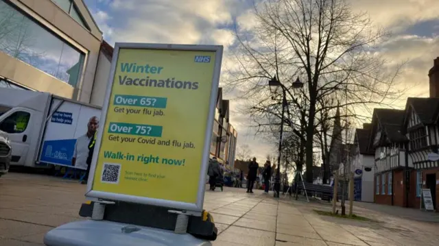 NHS sign on street outside surgery encouraging uptake of winter vaccinations