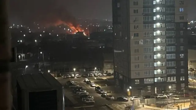 A fire is visible in the distance, with a smoke plume