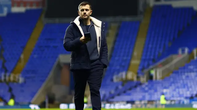 Jack Wilshere holds his phone while walking across the pitch at the Select Car Leasing Stadium