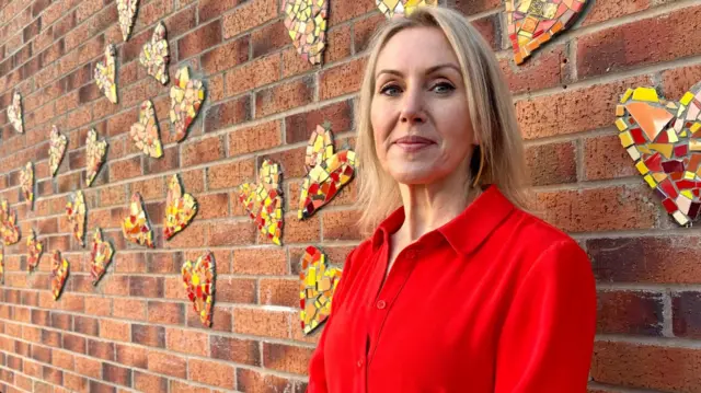 Head teacher Helen Stott stands in front of Covid memorial wall at school