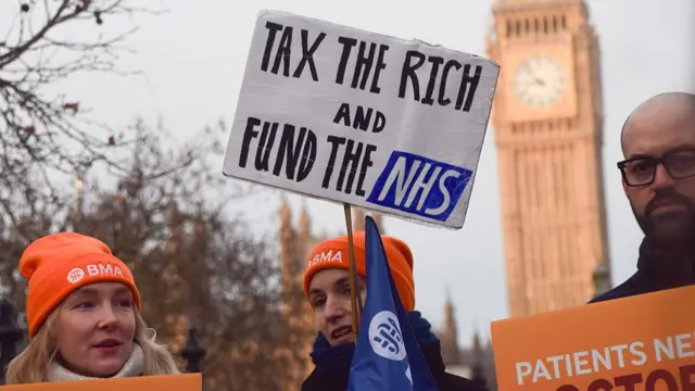 A doctor holds a 'Tax the rich and fund the NHS' placard as resident doctors, previously known as junior doctors, stand at the British Medical Association (BMA) picket outside St Thomas' Hospital