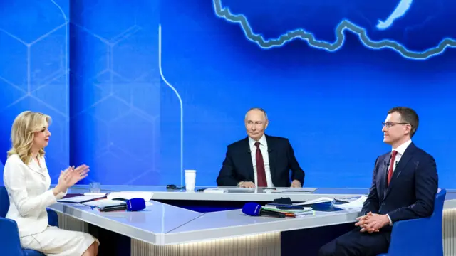Putin sits in between two presenters at national address