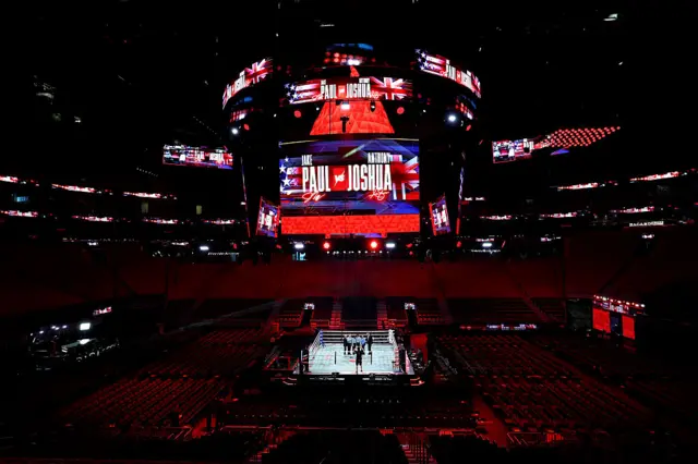 An empty arena with a large screen that says 'Paul v Joshua' above a boxing ring