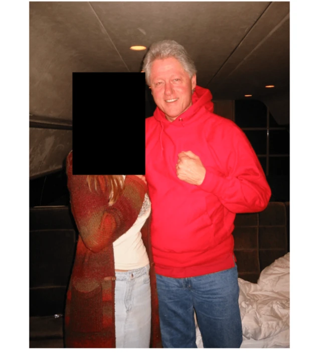 Former US President Bill Clinton (R) wears a red hoodie sweatshirt and jeans and poses with a woman also in a different red sweater and jeans whose face is redacted.