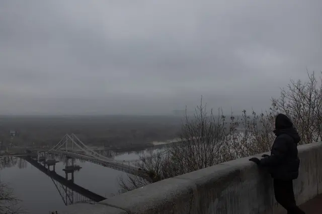 A woman looks out over the Dnipro River and the city skyline in Kyiv