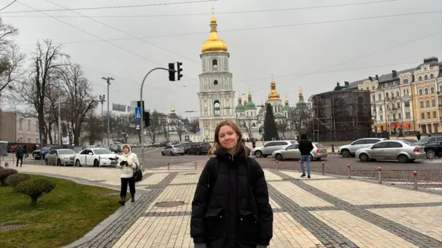 Yelyzaveta Horiaieva wears a black winter coat with Kyiv buildings in the background.