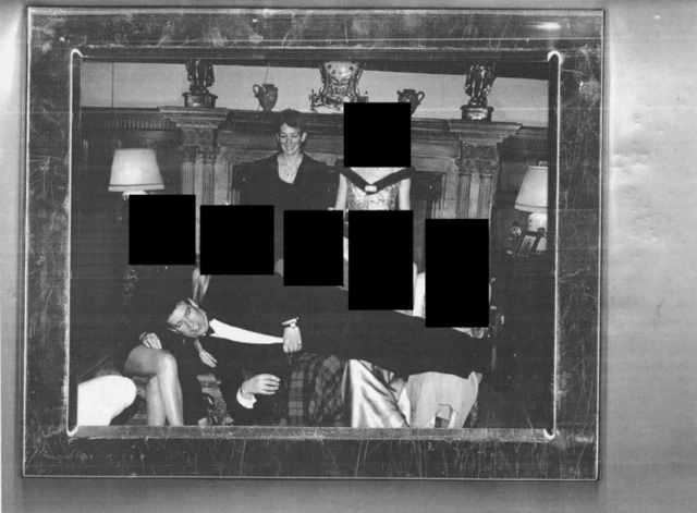 Andrew Mountbatten - Windsor lying across five women whose faces have been redacted. A woman with short hair stands behind, smiling.