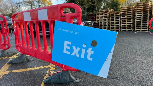 A red temporary barrier with a blue sign attached to it. The sign reads 'exit' and has a South East water logo.