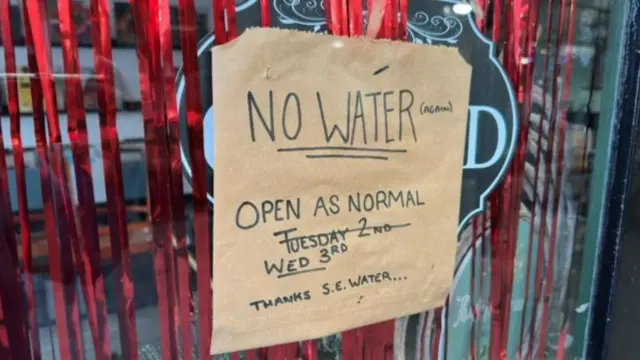 A sign on a door saying "NO WATER (AGAIN) THANKS SE WATER"