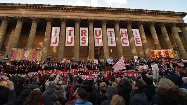 People hold football scarves at a vigil at St George's Hall in Liverpool