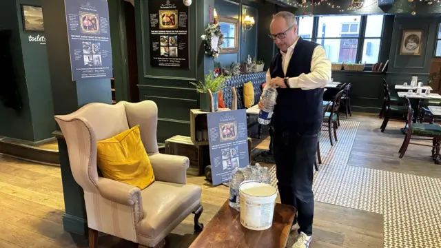Man in waistcoat filling up a water bottle in the lounge of a hotel