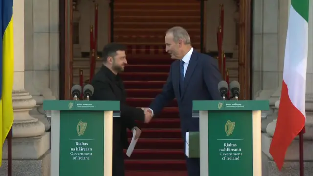 Zelensky and Martin shake hands while standing behind green podiums