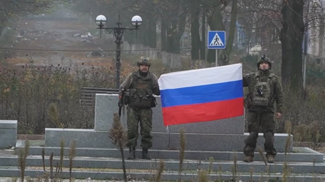 Image shows two Russian soldiers holding an unfurled Russian flag
