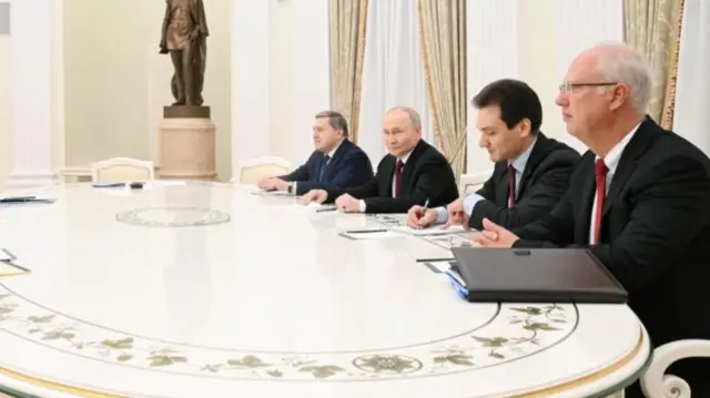 Four men sit at a table which is white and shiny