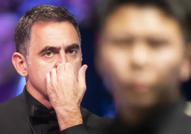 Ronnie O'Sullivan (left) watches on as Zhou Yuelong (right) is at the table