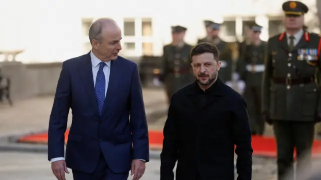 Zelensky and Martin walking through a street with Irish troops in military uniform behind them.