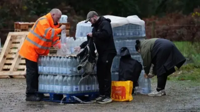 People collecting bottles of water from a car park