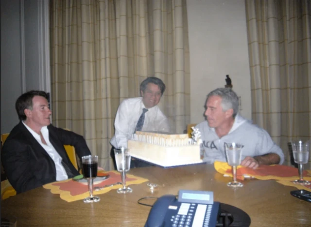 Peter Mandelson, an unidentified man and Jeffrey Epstein sit at a table with wine. Someone is presenting what appears to be a cake to the table.