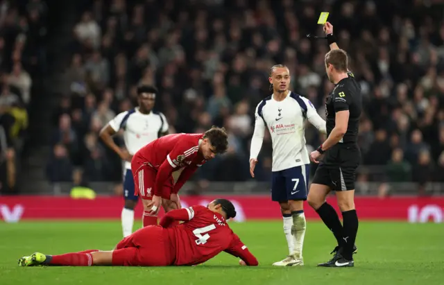 Tottenham Hotspur's Xavi Simons is shown a yellow card by referee John Brooks as Liverpool's Virgil van Dijk reacts after sustaining an injury