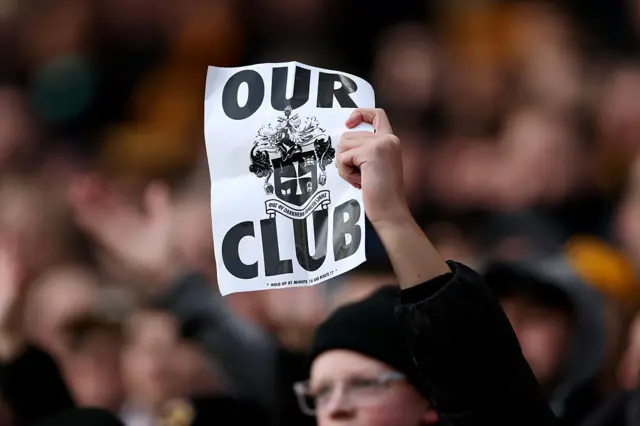 A Wolverhampton Wanderers fan holds a sign reading "our club"