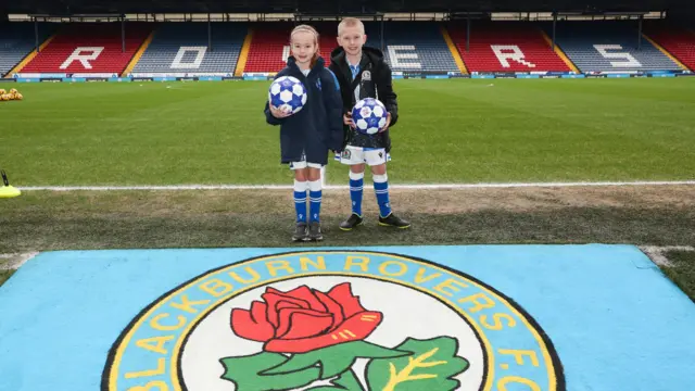 Two young mascots stand beside the Blackburn Rovers club crest at Ewood Park