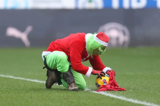 A man dressed as the Grinch puts a ball in a red bag