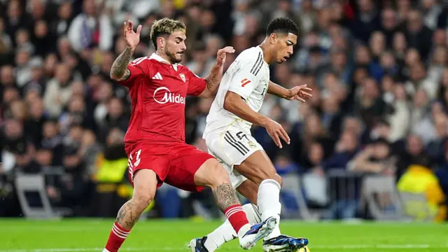 Jude Bellingham of Real Madrid is challenged by Isaac Romero o