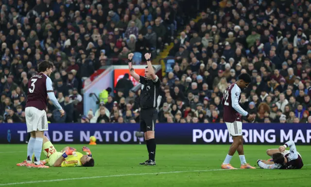 Aston Villa's Emiliano Martinez reacts after sustaining an injury as referee Michael Oliver looks on