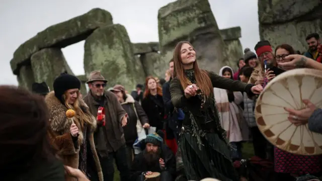 A crowd dances and plays instruments beside the monument
