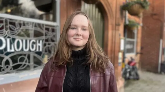 A young woman in a red leather jacket and strawberry blonde hair
