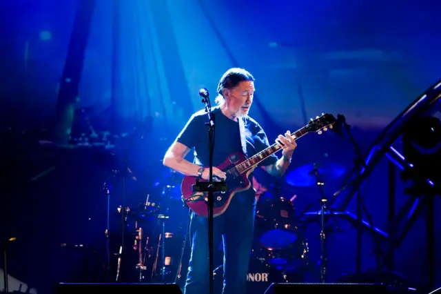 Chris Rea playing guitar on stage lit by dark blue lights