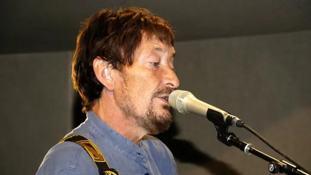 Chris Rea singing into a microphone - he is wearing a blue shirt