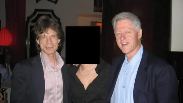 Mick Jagger poses in a pink shirt and dark suit next to a woman whose face has been redacted. Bill Clinton stands on the right-hand-side of her, wearing a light blue shirt and a dark suit