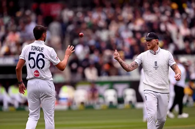England's captain Ben Stokes (R) tosses the ball to bowler Josh Tongue (L) on the first day