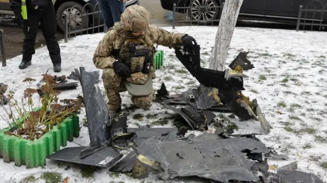 A man in camouflage gear holds a piece of debris in a snowy scene