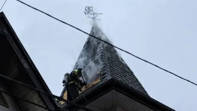 A smouldering rooftop where an emergency responder works