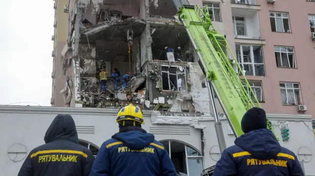 Three emergency workers survey the wreckage of an apartment building