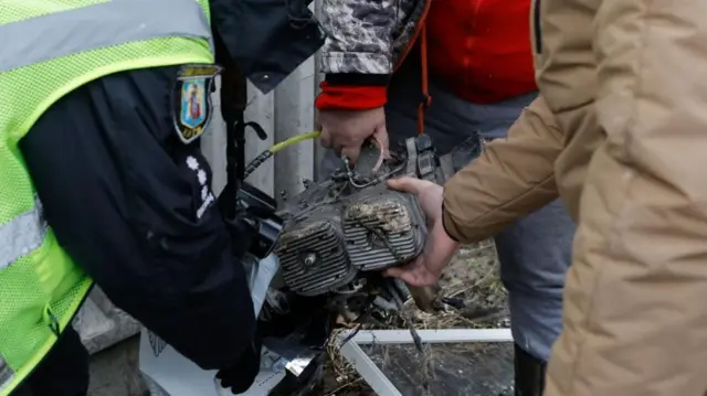 A metal device is held by three men who are placing it in a bag