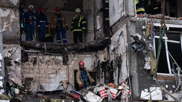 Rescue workers stand in rubble of building