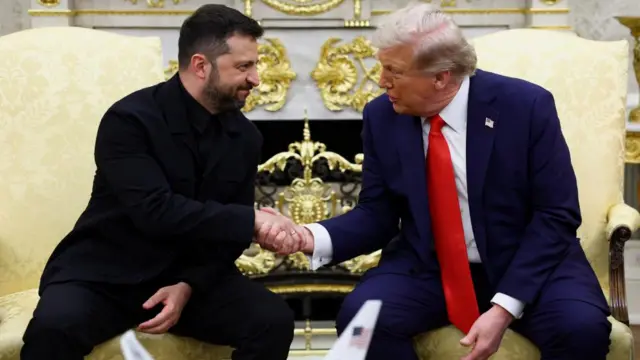 Volodymyr Zelensky and Donald Trump, both seated, shake hands while sitting on ornate, yellow chairs in the Oval Office.