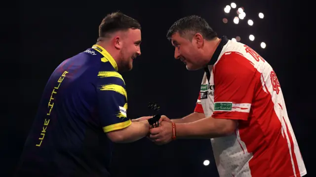 Luke Littler shakes hands with Mensur Suljovic