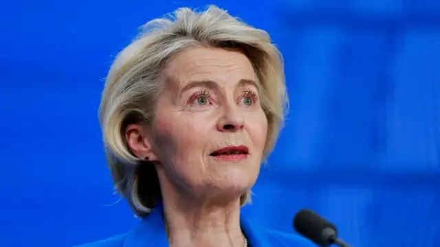Von der Leyen in a blue jacket at a podium in front of a blue screen
