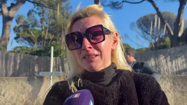 A woman in a black jumper and sunglasses cries