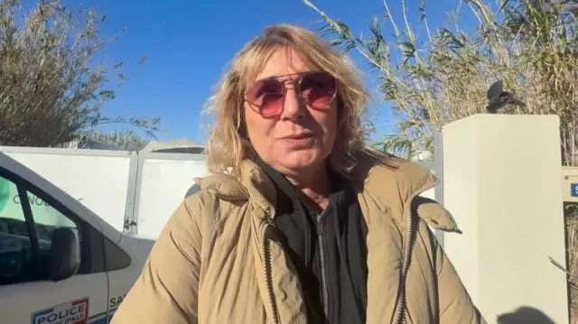 A woman with blonde hair and a beige coat on