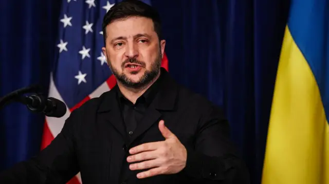 Zelensky speaking at a podium, illustrating a point with his hand